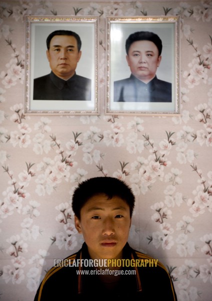 North Korean boy posing below the portraits of the Dear Leaders in his home, Kangwon Province, Chonsam Cooperative Farm, North Korea