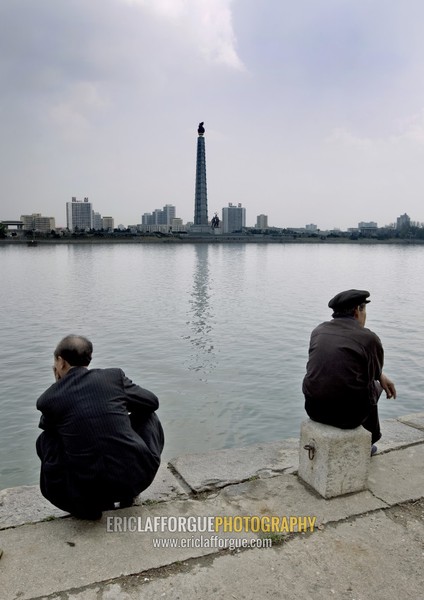 North Korean men sit in front of the Taedong river with the Juche tower in the background, Pyongan Province, Pyongyang, North Korea