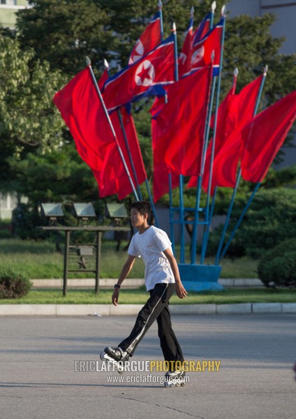 North Korean boy roller skating in front of red flags, Pyongan Province, Pyongyang, North Korea