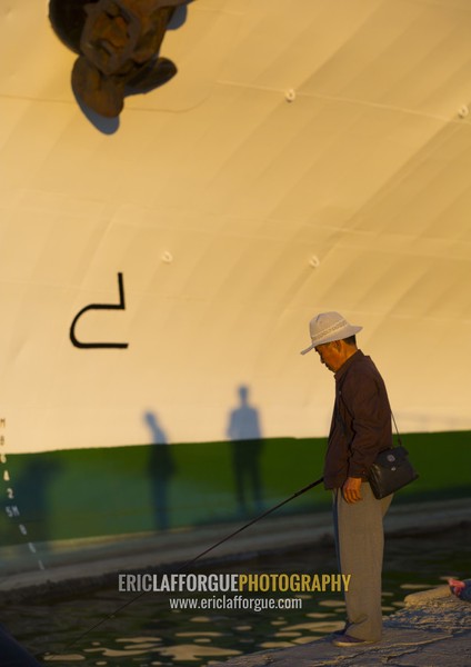 North Korean senior man fishing in the sea in front of a ship, Kangwon Province, Wonsan, North Korea